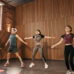 Group of adults doing jumping jacks in modern gym interior.